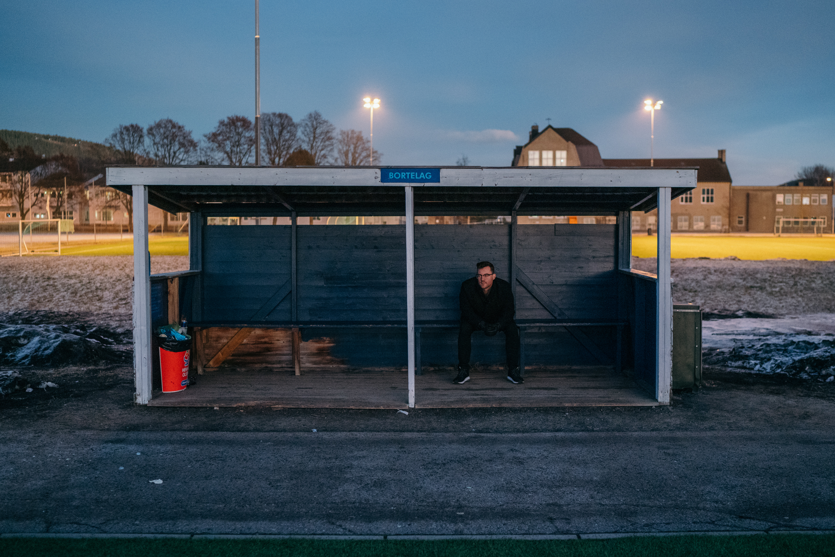 Bilde av Ole Tobias som sitter i et skur på en fotballbane.