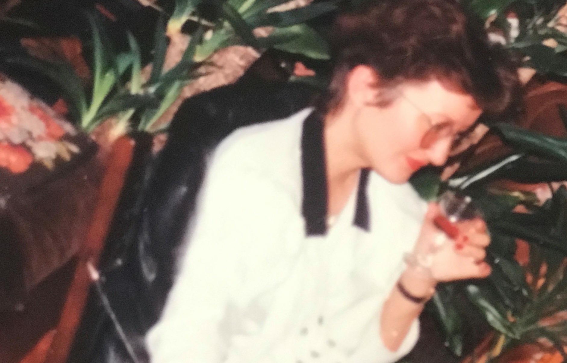 Bilde av Gunn-Helen som ung voksen. Hun sitter i en skinnstol, har briller og er ikledd en hvit overdel. I venstre hånd har hun et glass med vin.