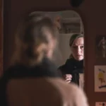 En preget, trist dame ser på seg selv i et speil.
