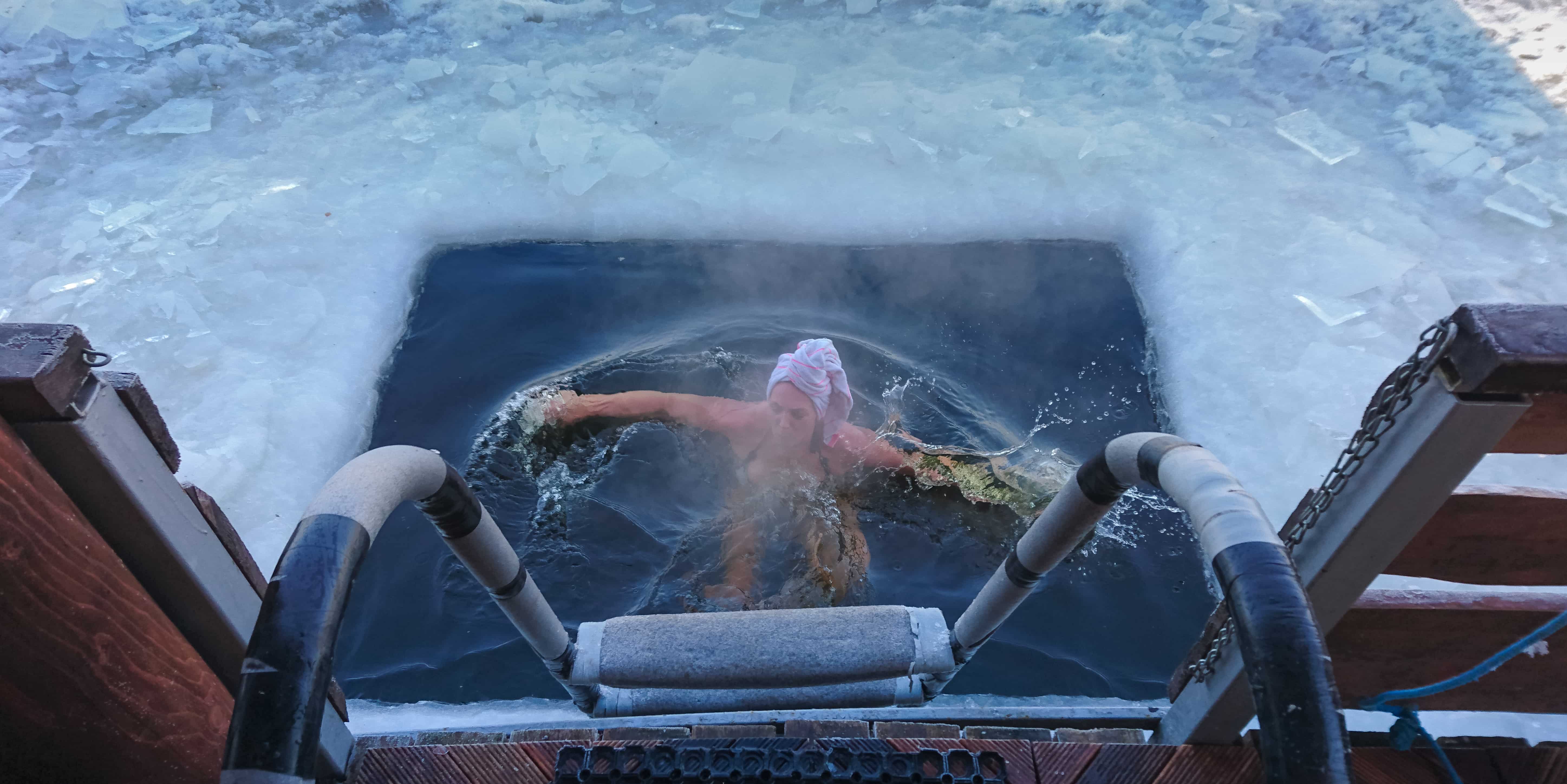 Kvinne som isbader i et hull i isen, sett fra toppen av badestigen. Foto.