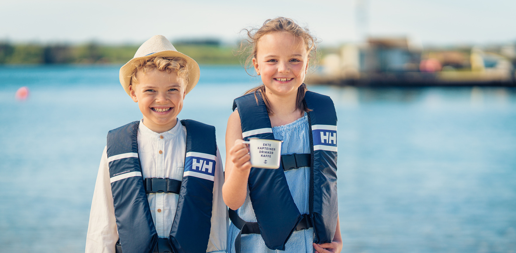 Isak og Ella som spiller hovedroller i kampanjefilmen står med vest og ekte kapteiner-koppen foran et blått hav