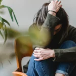 En ung dame som holder rundt knærne, ser ned og ser deprimert ut.