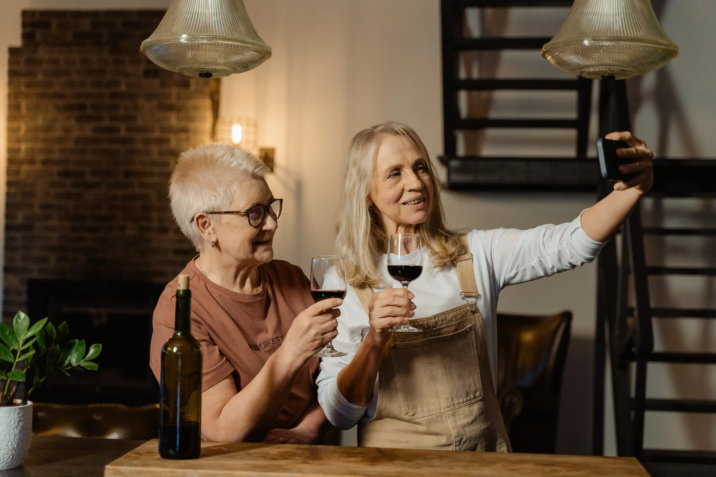 to eldre kvinner drikker vin og tar selfie med en mobil