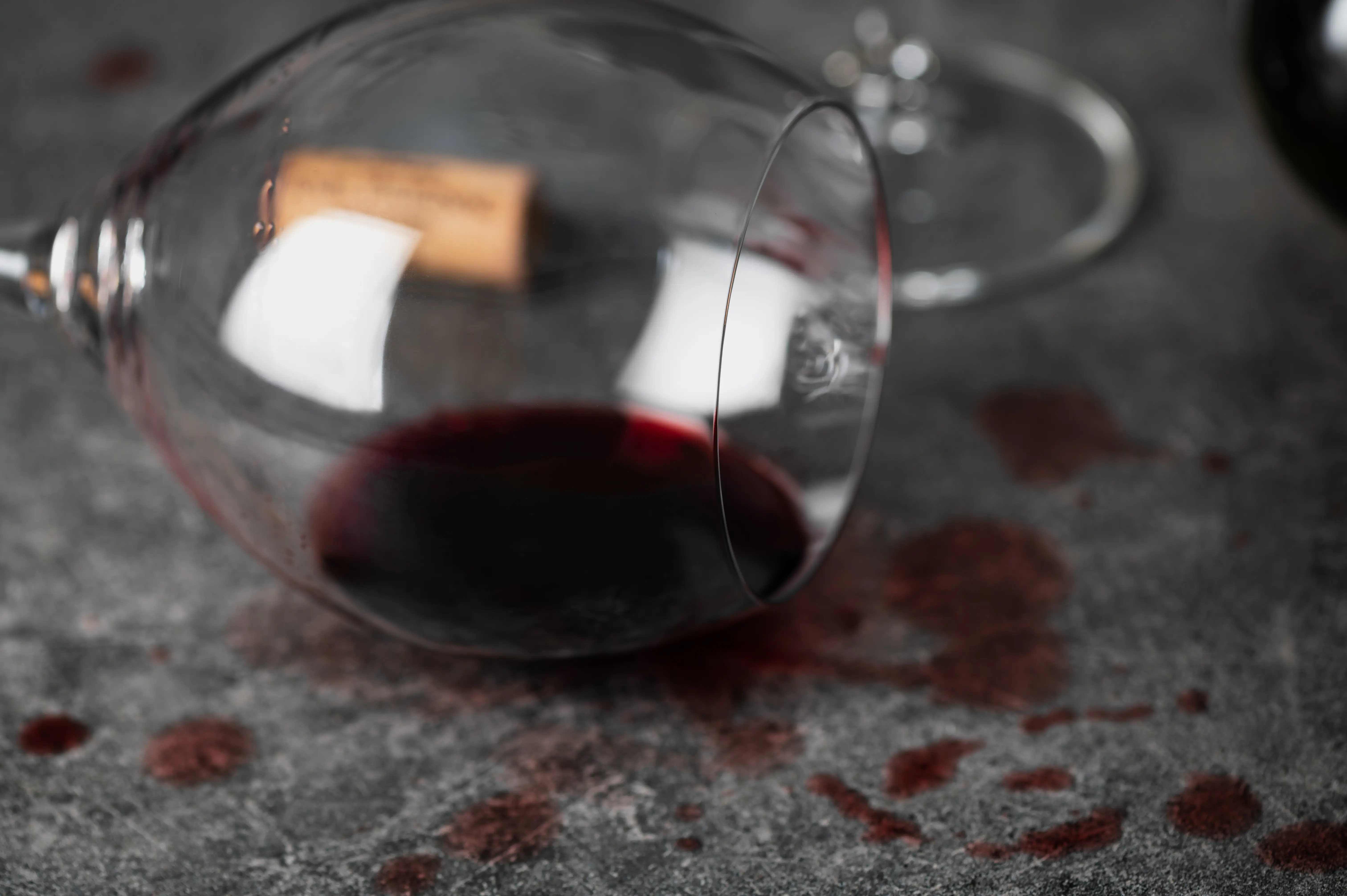 Et liggende rødvinsglass på en keramikkbenk. noe rødvin er sølt