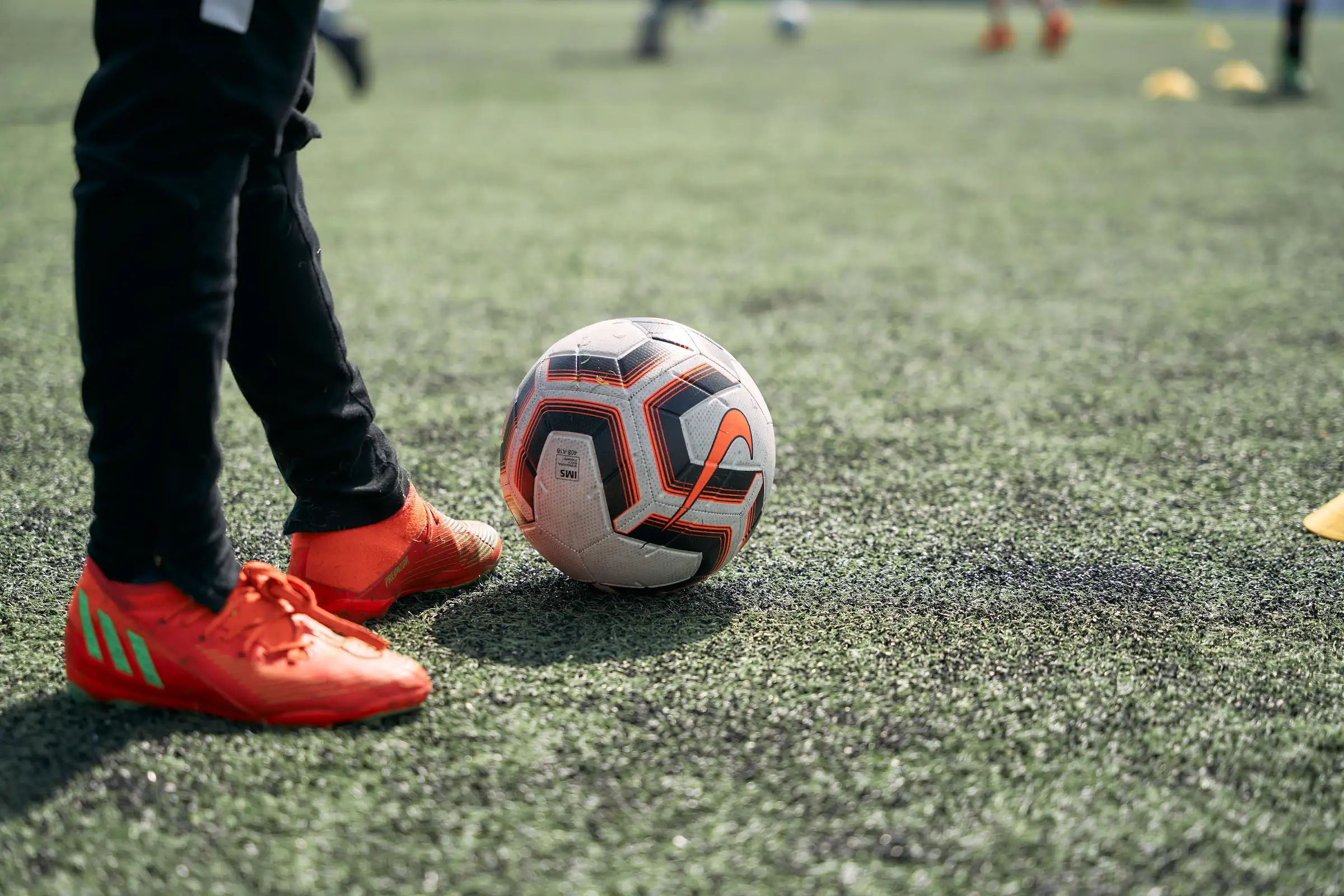 Bilde av en fotball og bein som står ved siden av på en kunstgressbane
