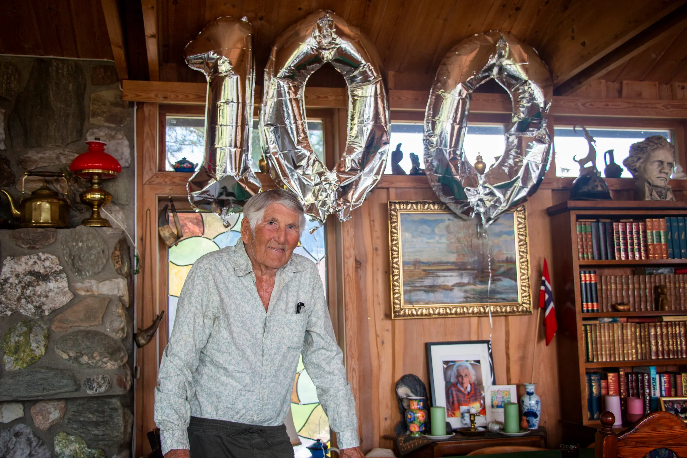 Ernst August Røgler står i sin egen stue med ballonger med form av 100