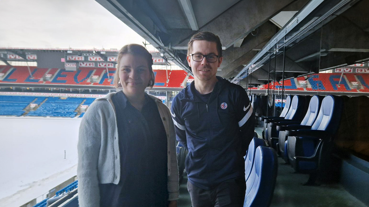 Ragnhild og Rasmus står på tribunen på ullevåll stadion og smiler til kamera.
